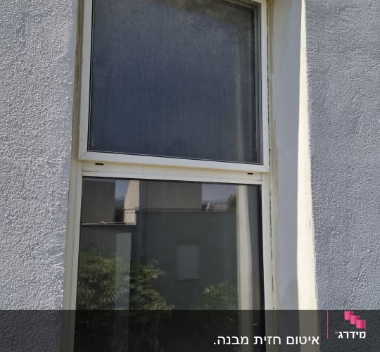 חלון עם מסגרת לבנה על קיר חיצוני אפור